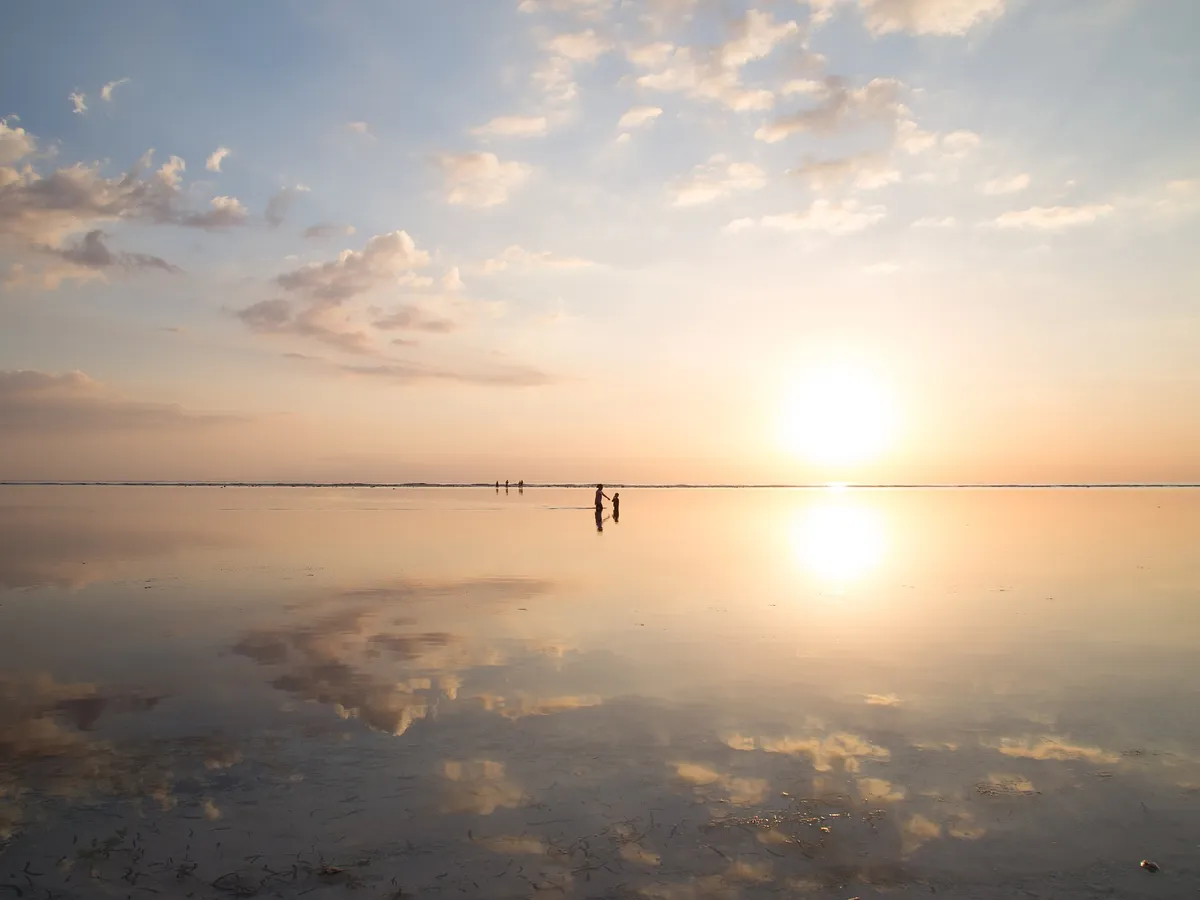 Roligt hav ved solnedgang, hvor himlen spejler sig blankt i vandet.